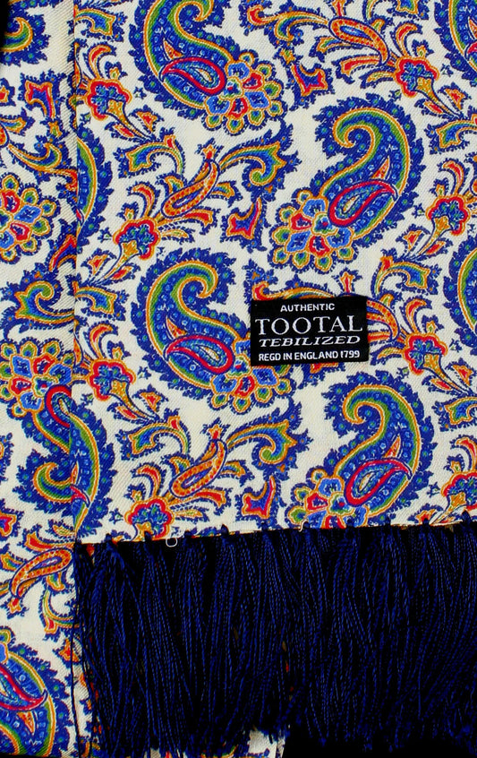 A close-up of a patterned scarf featuring a white base with a vibrant blue, red, and yellow paisley design, finished with a dark blue fringe at the bottom. A black brand label reading 'AUTHORISED TOOTAL TEBILIZED FREDO IN ENGLAND 1995' is visible.